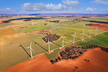 Elevated view of wind turbines in a row in a wind park with large shadows over an agricultural...