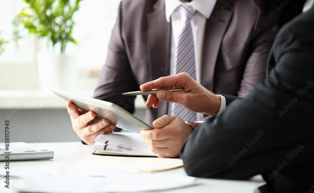 Wall mural two businessman are looking and studying statistics on tablet display closeup. male hand opponent ho