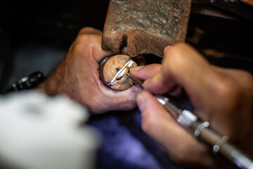 Jeweler hands setting a diamond into a ring with a burin in a jewelry workshop. Goldsmith working and creating a gold jewel. - obrazy, fototapety, plakaty