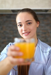 Young beautiful attractive girl in pajamas in the kitchen drinking orange juice holding a glass in her hand