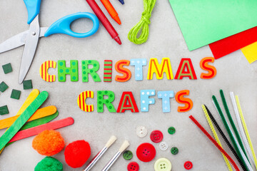 Christmas crafts in bright lettering with colorful craft supplies on a mottled grey surface