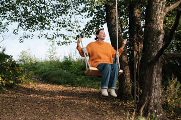 Adorable young woman swinging on swing in park in autumn