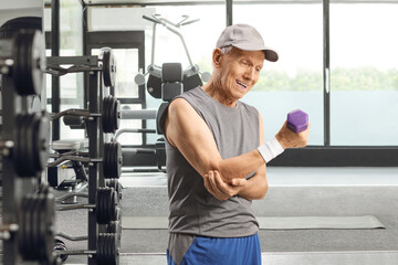 Elderly man in sportswear with elbow pain exercising with a dumbbell