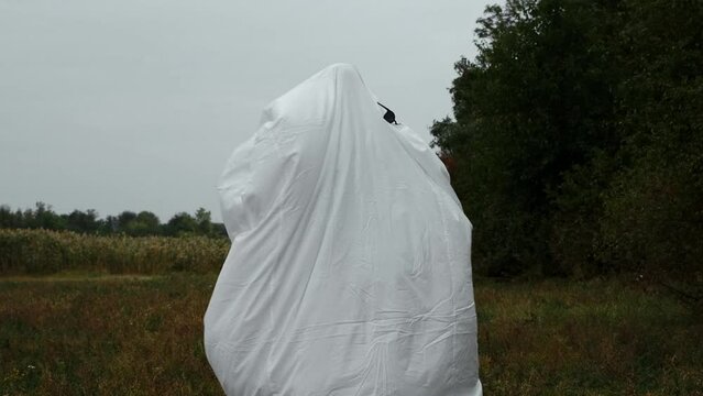 Creative Halloween costume for an adult. A ghost of a white sheet with black sunglasses dancing in an autumn field. 4k horizontal slow motion footage