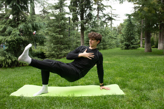 Man doing yoga in the park on the sunny morning. Fit young man exercising outdoors on yoga mat Healthy and active lifestyle concept. Training outdoors. 