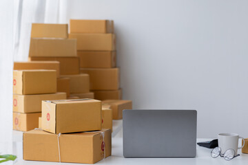 Parcel boxes on shelf and color shopping bags placing near laptop on table. SME business on shopping online at home office packaging on background is popular business.
