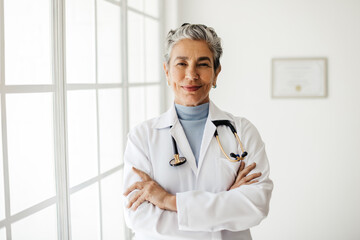 Confident in her experience and expertise, mature female professor stands in her office with her arms crossed