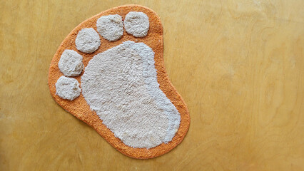 Funny fluffy rug in the shape of a foot on a beige wooden floor.