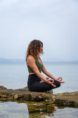 Fototapeta na wymiar Woman practicing yoga by the sea on the rocks. Padmasana - Lotus pose - meditation sitting - chin mudra