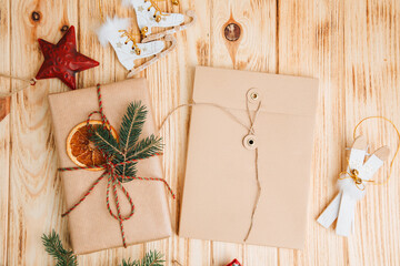 Background for greetings. Gift wrapping in brown paper with dry orange and branch of coniferous tree and Christmas toys on a light wooden background. Top view