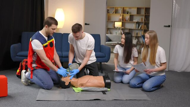 First aid measures for victims. Basic emergency training in group, man showing artificial lung ventilation on mannequin, indirect heart massage
