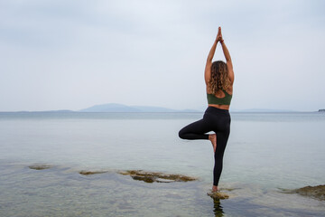 Woman practicing yoga by the sea on the rocks. Vrksasana - Tree pose