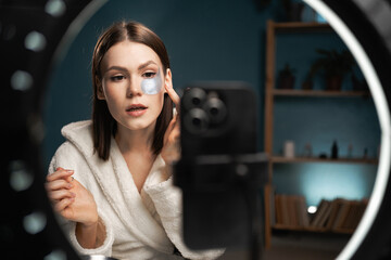 Girl making make-up tutorial on mobile phone at home in the evening. A young female is applying eye...