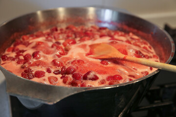 Cooking strawberry jam in a large bowl at home. Wooden spoon in a bowl with jam