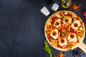 Funny creepy Halloween pizza with eyes made from cheese, tomatoes and olive. Halloween party food idea, creative recipe of margarita pizza top view copy space