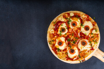 Funny creepy Halloween pizza with eyes made from cheese, tomatoes and olive. Halloween party food...