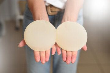 Woman showing breast augmentation implants in her hands - obrazy, fototapety, plakaty