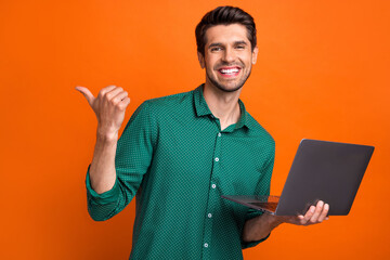 Photo of candid young positive guy brunet hair directing finger mockup all options his service laptop isolated on orange color background