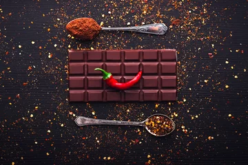 Keuken spatwand met foto Dark chocolate bar, red hot chilli pepper cayenne,  dry hot chili spices, cocoa beans nibs powder, food tasty design on black wooden background © ValentinValkov