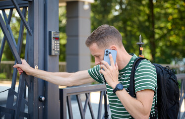 Man opens the gate to yard. Young male calling owner to ask code. Curious tourist trying to open gate to hotel. Ivano-frankivsk, Ukraine - 09.07.2023