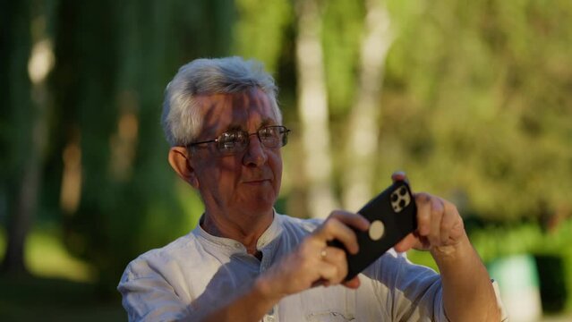 An old gray-haired man takes a selfie on a mobile phone