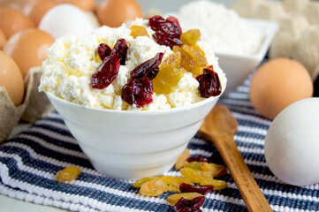 Bowl of cottage cheese with cranberries and raisins, eggs, flour. Ingredients for making cheesecakes and cheese casseroles. - obrazy, fototapety, plakaty