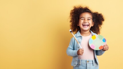 Happy child holding a palette and paintbrush - obrazy, fototapety, plakaty