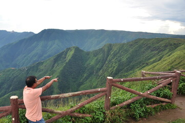 Amidst the serene beauty of Laitlum Canyon in Meghalaya, Northeast India, a joyful tourist stood in admiration. With an outstretched arm, they pointed towards the distant hills.