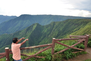 Fototapeta na wymiar Amidst the serene beauty of Laitlum Canyon in Meghalaya, Northeast India, a joyful tourist stood in admiration. With an outstretched arm, they pointed towards the distant hills.
