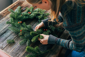 A woman decorates a Christmas wreath made of natural fir branches.
