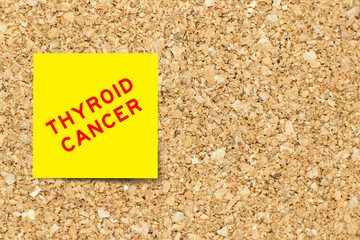 Yellow note paper with word thyroid cancer on cork board background with copy space