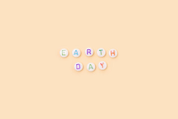 Obraz premium Earth Day. Quote made of white round beads with colorful letters on a beige background.