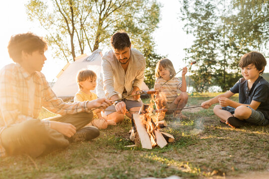 Father and children roasting sausages together in bonfire at picnic