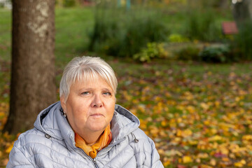 Elderly woman sits on a park bench and enjoys a warm autumn day in the sun