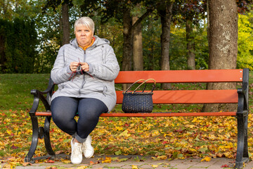 Elderly woman sits on a park bench and enjoys a warm autumn day in the sun