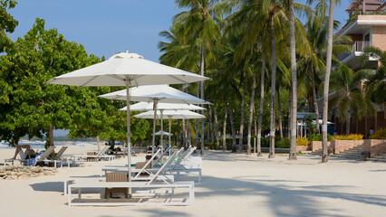 sandy beach with comfortable sun beds and umbrellas on a tropical island, on a sunny day, calm