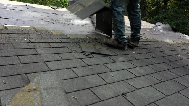 Closeup view of roofer removing old roof shingles to be replaced with new roof in house renovation project