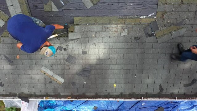 Overhead aerial view of roofer removing old roof shingles to be replaced with new roof in house renovation project