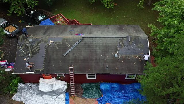 Aerial view of laborers removing old roof shingles to be replaced with new roof in house renovation project