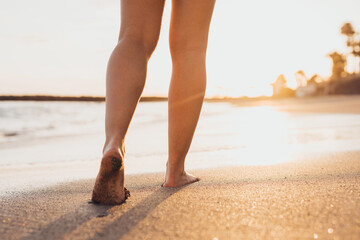 Beach travel - woman walking on sand beach leaving footprints in the sand. Closeup detail of female feet and golden sand on Tenerife beach.
 - obrazy, fototapety, plakaty