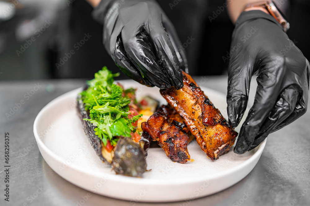 Sticker chef cooking of grilled pork ribs with baked eggplant at the restaurant kitchen