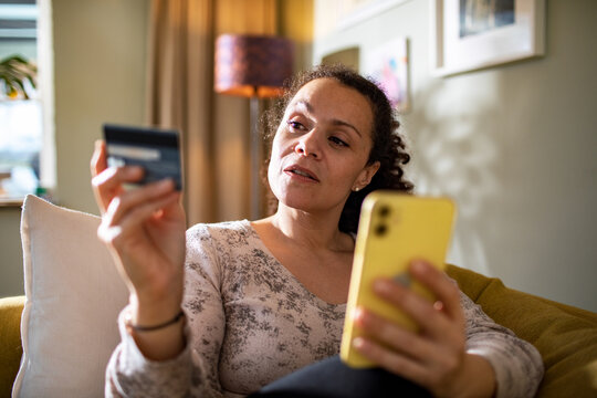 Young mixed woman online shopping from her smartphone on the couch at home