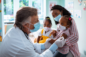 Senior pediatrician preparing a young child for vaccination in the clinic