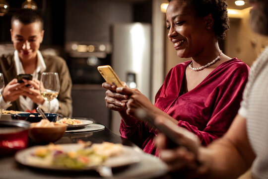 Young woman receiving a text on her smartphone while having dinner with her friends at home