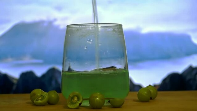 Pouring green Amla juice into the white glass, sky background, Indian gooseberry . Natural ayurbedic indian gooseberry. Green juice isolated raw amla into the wooden table. 