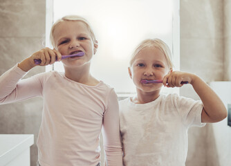 Children, brushing teeth and a girl with her sister in the bathroom of their home together for oral hygiene. Portrait, dental cleaning and siblings using a toothbrush in the morning for mouth care