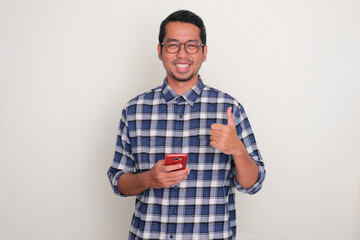 Adult Asian man smiling and give thumb up while holding mobile phone