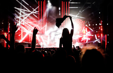 Fototapeta na wymiar Stage lights against a happy woman with raised arms while enjoying a concert at a music festival