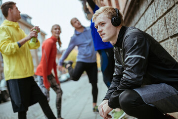 Obraz premium Young man listening to music on his headphones while getting ready to run with his friends in the city