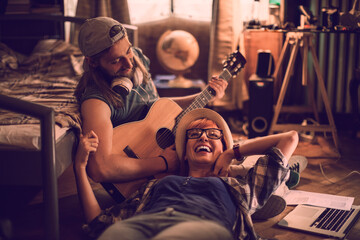 Young couple playing guitar and singing together on the floor of their apartment